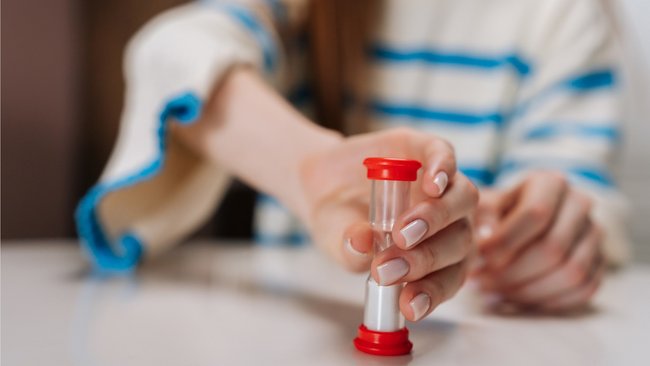 Gezeigt wird eine Frau, die eine Sanduhr umdreht.