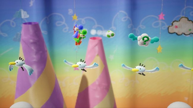 Der -Screenshot aus dem Spiel Yoshi's Crafted World zeigt eine fliegende Yoshi-Figur, die ein grünes Ei wirft. Die Szene ist in einer handgemachten Welt in Häkel-Optik mit pastellfarbenen Bergen und einem Himmel mit Wolken und Sternen angesiedelt. Mehrere fliegende Vögel und eine schwebende Wolke mit einem Fragezeichen sind ebenfalls zu sehen.