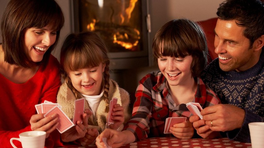 Eine Familie spielt vor einem Kamin zusammen ein Kartenspiel.