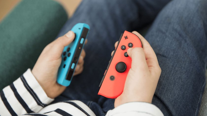 Gezeigt werden die Hände eines Kindes in Nahaufnahme, die die Controller der Konsole Nintendo Switch halten, während das Kind auf einem Sofa sitzt.