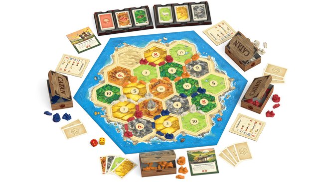 Gezeigt wird das Spielmaterial der Catan-Version 2025. Um das Spielbrett, das aus zahlreichen Hexagonen besteht, sind Karten, Pappschachteln mit Spielfiguren und ein Paar Würfel verteilt.