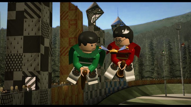 Das Bild zeigt eine Szene aus dem Videospiel LEGO Harry Potter Collection. Im Vordergrund fliegen zwei LEGO-Figuren auf Besen: links eine Figur in grüner Quidditch-Uniform (vermutlich ein Slytherin-Spieler) mit einem besorgten Gesichtsausdruck, und rechts eine Figur mit schwarzen Haaren, Brille und roter Quidditch-Uniform (erkennbar als Harry Potter). Im Hintergrund sind die Quidditch-Tribünen mit bunten Bannern und Fahnen zu sehen, sowie ein Waldgebiet und Berge in der Ferne. Rechts im Bild sind Quidditch-Torringe erkennbar. Die Szene stellt offensichtlich ein Quidditch-Spiel auf dem Hogwarts-Gelände dar, umgesetzt im charakteristischen LEGO-Videospiel-Stil.