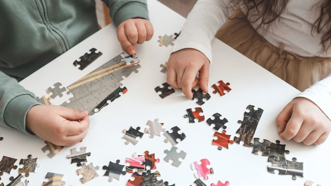 Gezeigt werden die Hände von zwei Kinder, die ein Puzzle zusammensetzen.