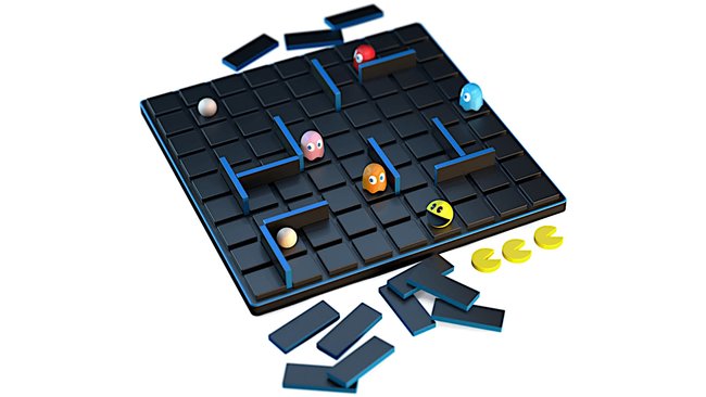 Das Bild zeigt ein PAC-MAN-Brettspiel. Das Spielfeld besteht aus einem Gitter aus schwarzen und blauen Quadraten, auf dem mehrere Trennwände platziert sind, um ein Labyrinth zu bilden. Auf dem Spielfeld befinden sich Spielfiguren, darunter PAC-MAN und die vier Geister aus dem Originalspiel: Blinky (rot), Pinky (pink), Inky (blau) und Clyde (orange). Zusätzlich sind einige gelbe PAC-MAN-Spielfiguren und weiße Kugeln auf dem Spielfeld verteilt. Außerhalb des Spielfelds liegen weitere Trennwände, die wahrscheinlich verwendet werden können, um das Labyrinth zu verändern.