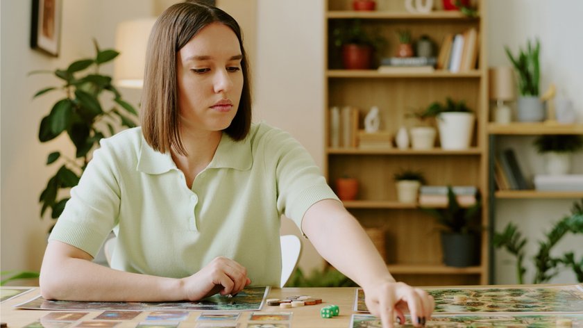 Gezeigt wird eine junge Frau, die alleine ein Brettspiel spielt.