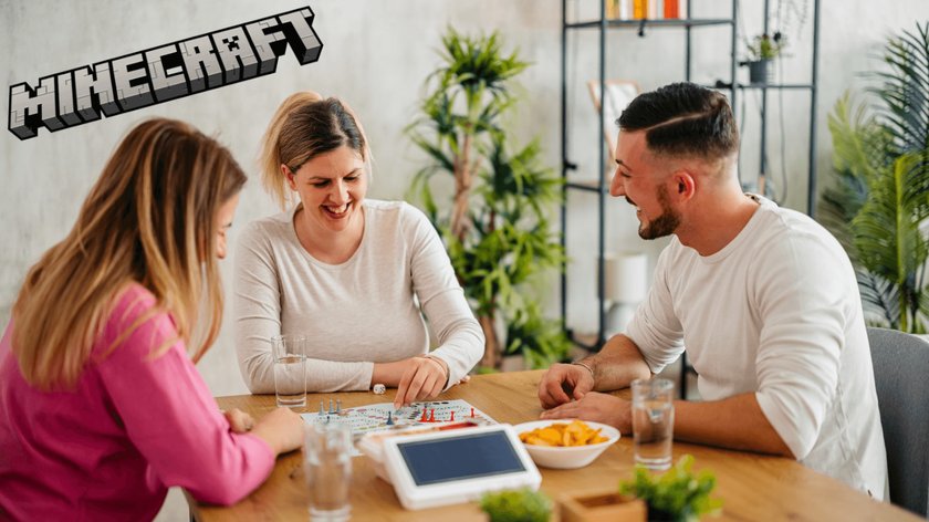 Gezeigt wird eine Spielrunde bestehend aus zwei Frauen und einem Mann von je ca. 30 Jahren, die ein Brettspiel an einem Tisch in einen Wohnzimmer spielen. Es stehen auch Snackschalen und Pflanzen auf dem Tisch. In der oberen linken Ecke ist das Minecraft-Logo zu sehen.