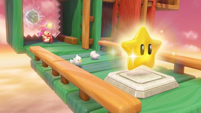 Das Bild zeigt eine Szene aus dem Videospiel "Captain Toad: Treasure Tracker". Im Vordergrund ist ein leuchtender gelber Stern auf einer Plattform zu sehen. Im Hintergrund befindet sich die Spielfigur Toadette, die gerade durch ein Leveltor kommt. Die Umgebung besteht aus farbenfrohen Holzplanken und Balken, die eine schwebende Struktur bilden. Zwei kleine weiße Vögel sind ebenfalls auf der Plattform zu sehen. Der Himmel im Hintergrund ist rosa-orange, was auf eine Sonnenuntergangsstimmung hindeutet.