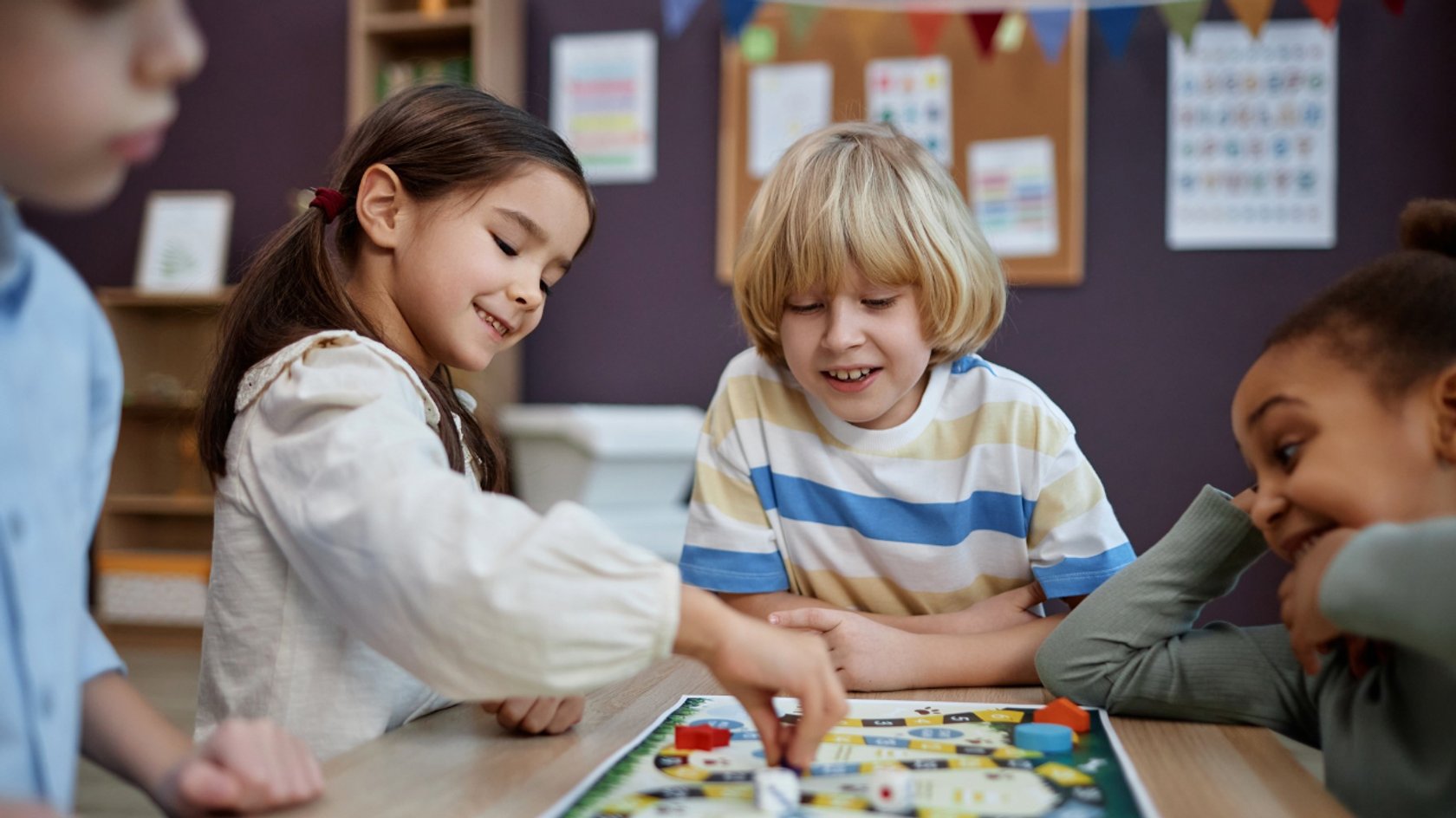 Gezeigt wird eine Gruppe von vier Kindern, die ein Brettspiel spielt.