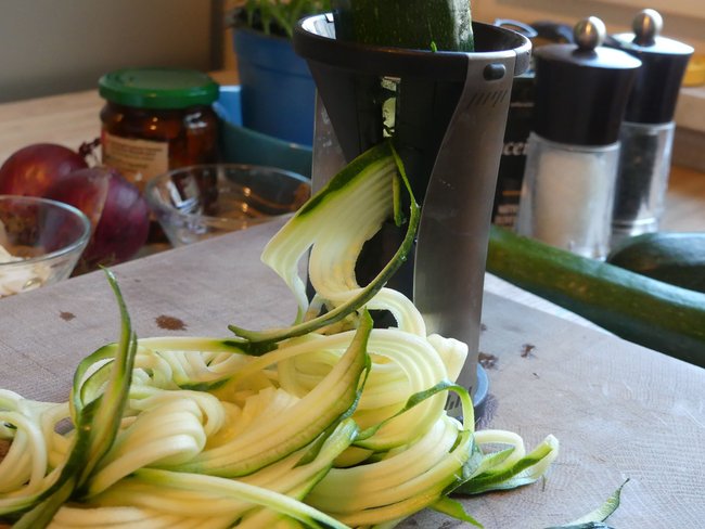 Das Bild zeigt eine Nahaufnahme eines Spiralschneiders, in dem eine Zucchini gedreht wird, um Zucchininudeln zu erzeugen.