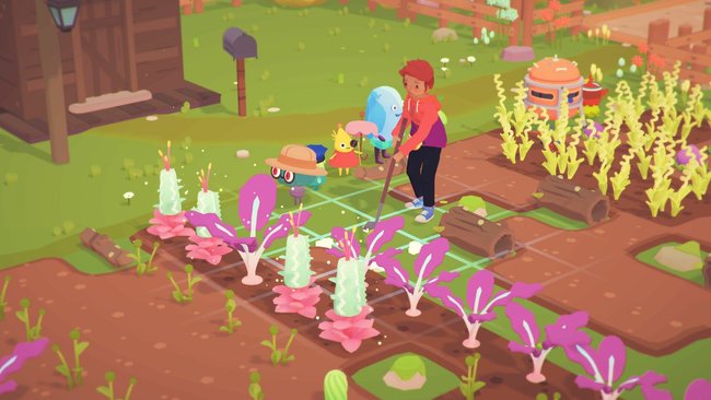 Gezeigt wird eine Szene aus dem Videospiel Ooblets, in dem eine Frau einen Garten mit Gemüsebeeten pflegt. Neben ihr stehen einige kleine, bunte Monsterfiguren.